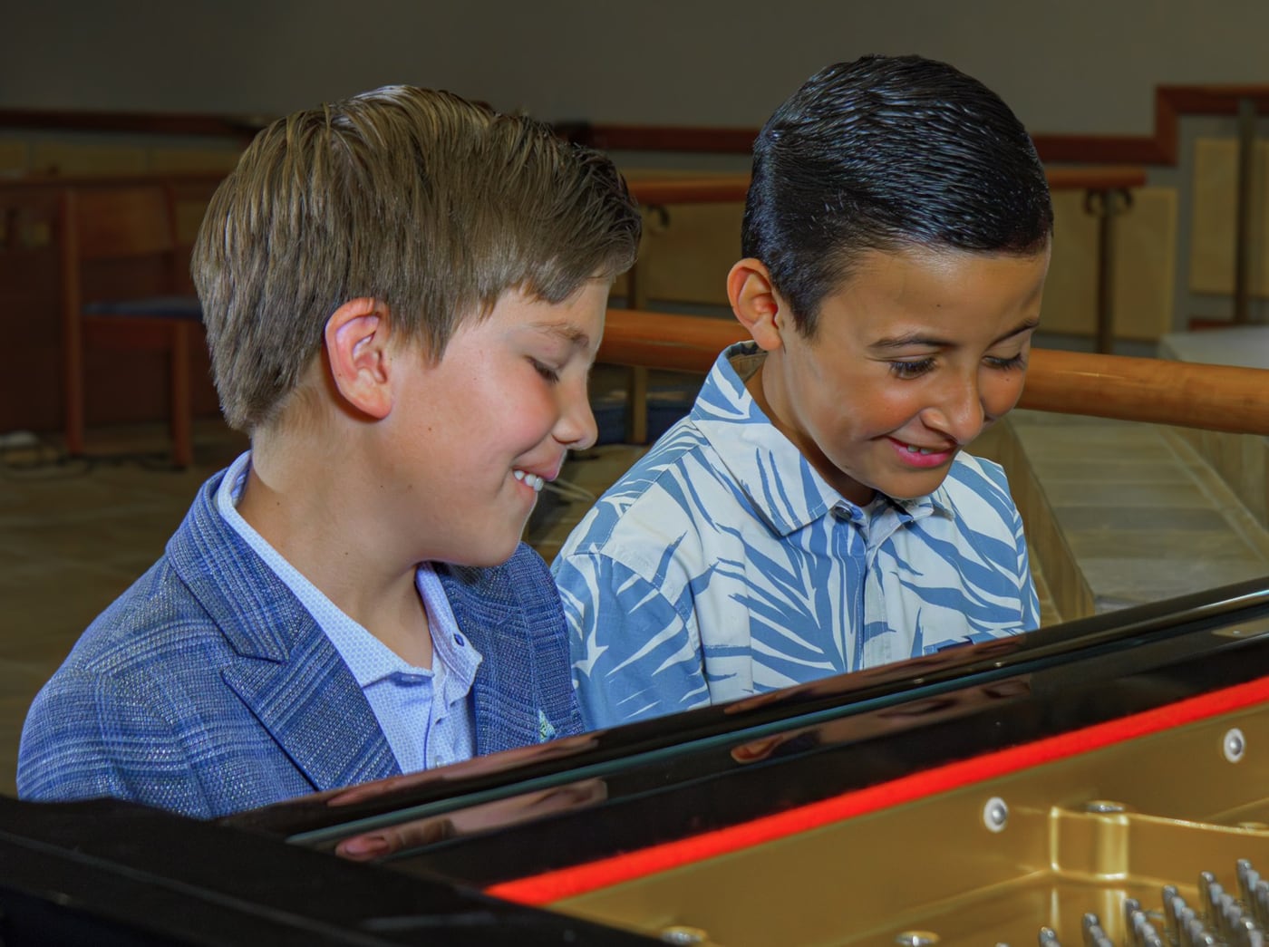 Two boys leaning over the open lid of a grand piano, both grinning, at a Player One recital.