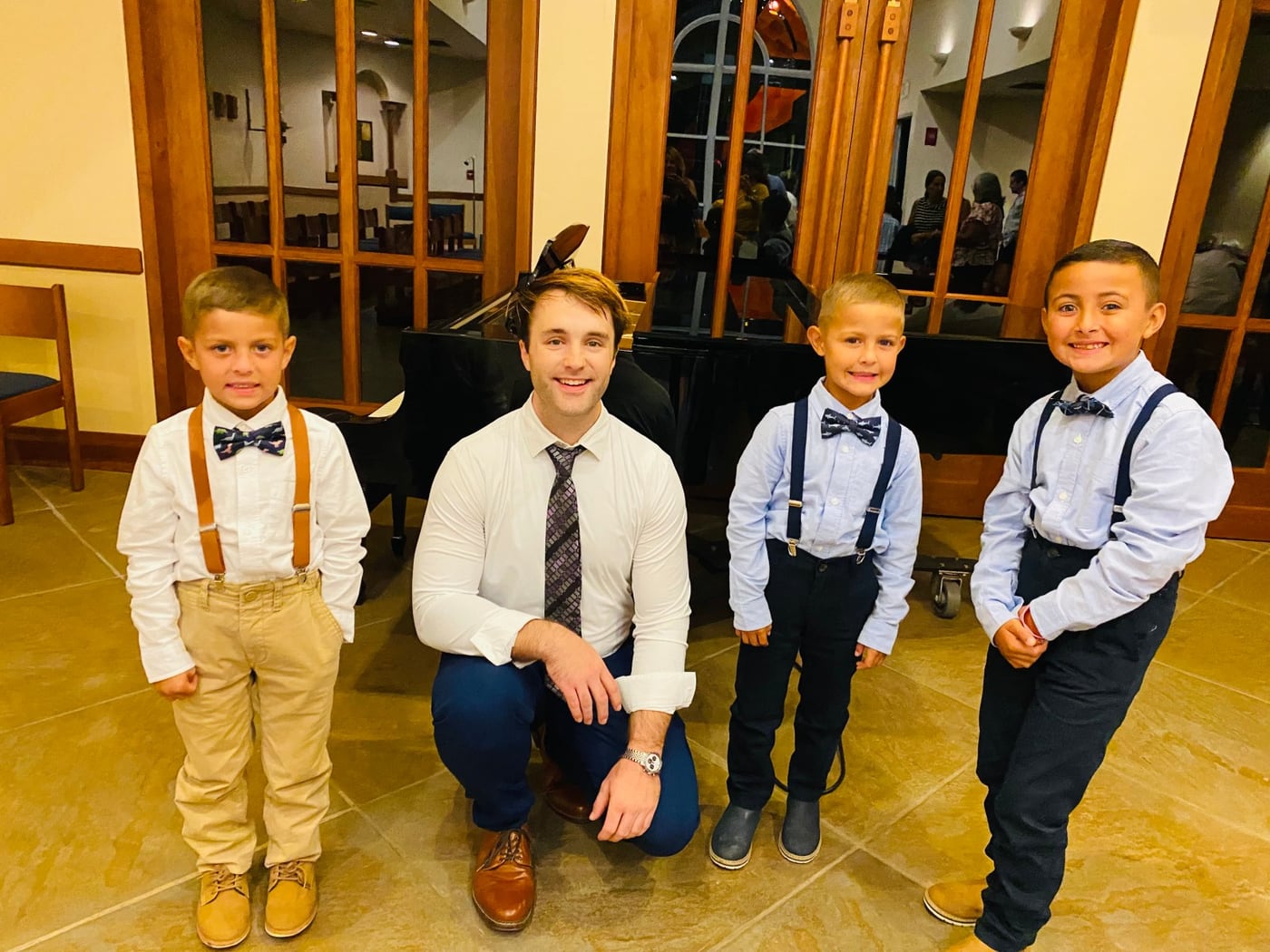Evan Kliewer kneeling beside three young students in bow ties after their recital.