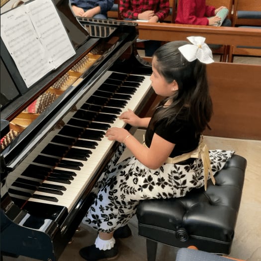 A young student at the grand piano, mid-phrase, in the recital hall.