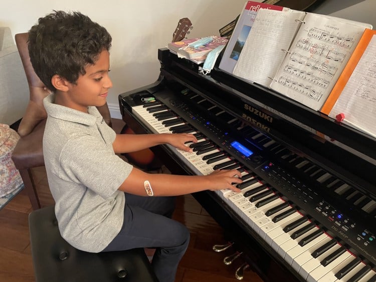 A student playing a digital piano at home with his assignment sheets open above the keys.